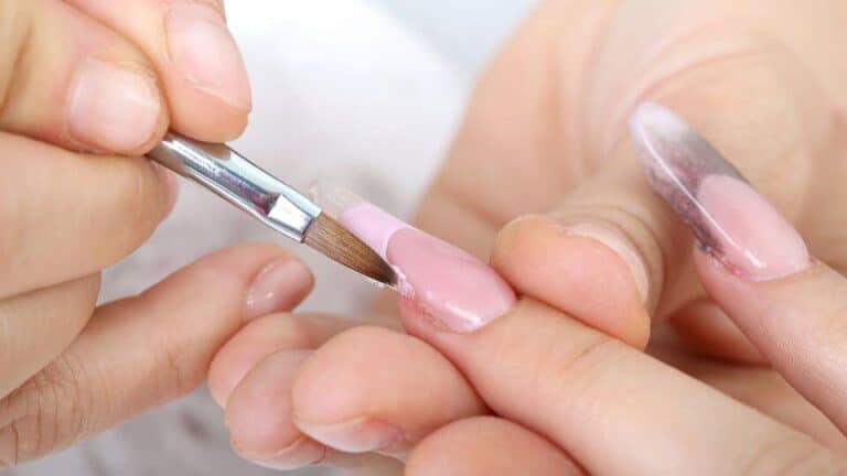 Detalle de una uña rosa pastel con un pincel aplicando esmalte en un salón de belleza en Bogotá